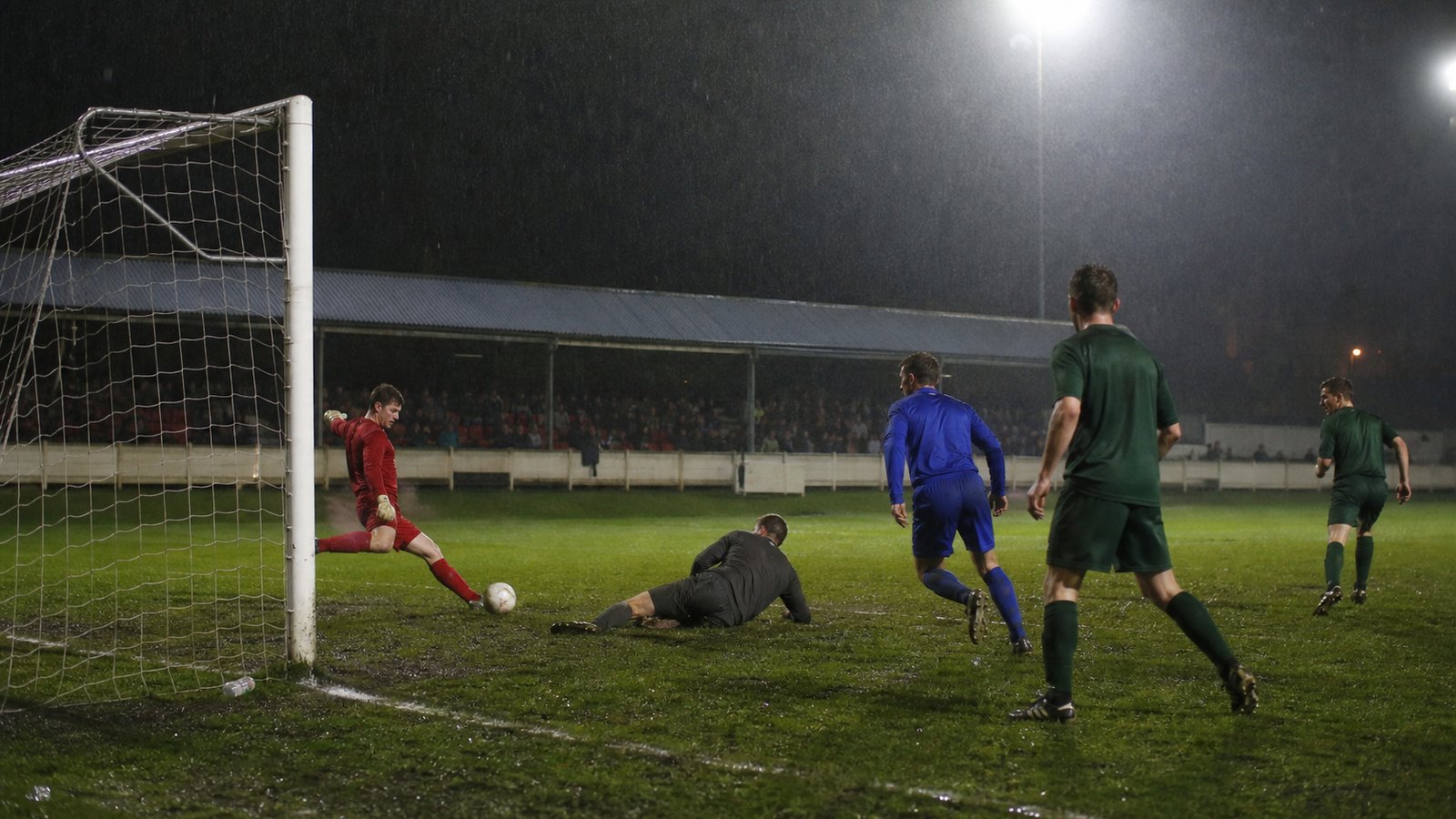 A fictional goalkeeper in red strikes a loose ball from close range after a crowded last-minute corner